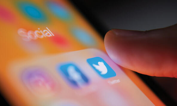 close up photo of a mobile phone screen with social media icons and a thumb about to press one